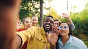 Point of view shot of cheerful students making online video call in park calling friends holding device looking at camera and talking gesturing waving hands