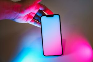 Hand holding smartphone. Blank screen mockup neon glow light.