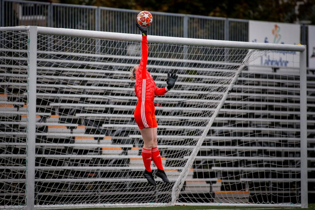 The soccer goalkeeper jumps up and tips the football over the crossbar of the soccer goals.