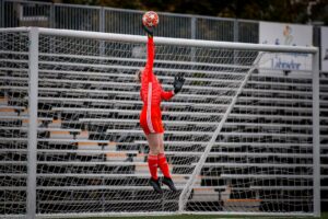 The soccer goalkeeper jumps up and tips the football over the crossbar of the soccer goals.