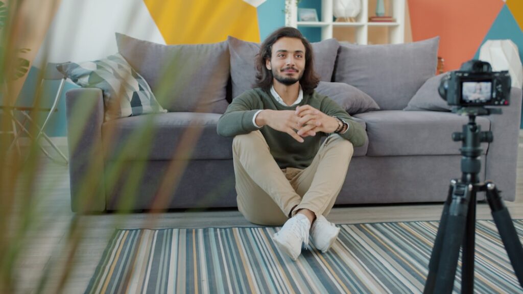 Happy Arab man is recording video for internet blog speaking and gesturing sitting on floor at home. Vlogging, youth and modern technology concept.