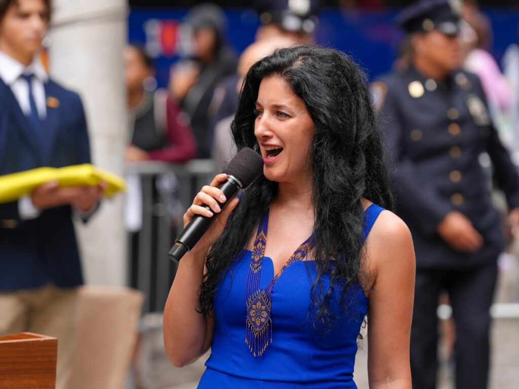 A Ukrainian rally unfolds in downtown Manhattan, where community members, NYC officials, and uniformed police gather in solidarity. A woman draped in a blue and yellow flag stands solemnly among the crowd, while a young attendee holds a folded Ukrainian flag during a formal civic ceremony. The event reflects unity, patriotism, and public support for Ukraine in the heart of New York City. Captured by Olek Buzunov @buzunov.photoart, documenting moments of resilience and civic engagement.
