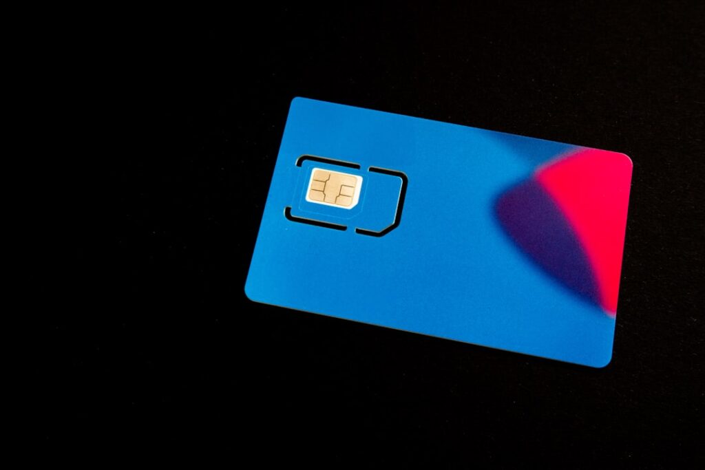 This image captures a single blue SIM card with a visible gold chip and a perforated micro SIM section ready to be detached. The card’s sleek design features a modern blue gradient fading into pink, set against a stark black background to emphasize its form and color. The photo highlights the important technology element that connects mobile phones to cellular networks, ideal for telecommunications, technology marketing, or mobile service-related visuals. The isolated, minimalistic setting creates a professional mood, suitable for use in advertising or editorial articles about mobile.