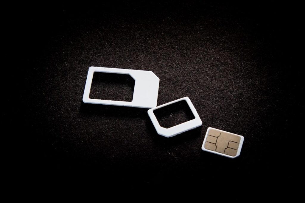 This image showcases the evolution of SIM cards, featuring three different sizes: the traditional standard SIM frame, the micro SIM frame, and the smallest, a nano SIM card. These components are essential for mobile connectivity in smartphones, enabling access to cellular networks and the internet. The stark black background emphasizes the progression in SIM card technology, highlighting compactness and modernization in mobile telecommunications. The visual demonstrates the shift toward smaller SIM formats that allow more space for advanced smartphone technologies and internet capabilities.