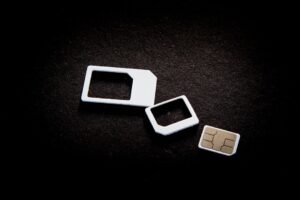 This image showcases the evolution of SIM cards, featuring three different sizes: the traditional standard SIM frame, the micro SIM frame, and the smallest, a nano SIM card. These components are essential for mobile connectivity in smartphones, enabling access to cellular networks and the internet. The stark black background emphasizes the progression in SIM card technology, highlighting compactness and modernization in mobile telecommunications. The visual demonstrates the shift toward smaller SIM formats that allow more space for advanced smartphone technologies and internet capabilities.